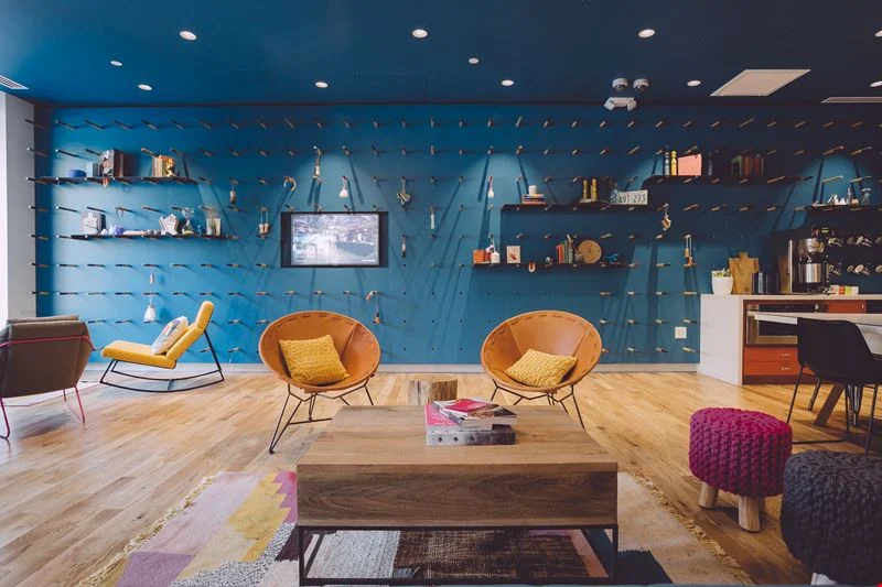 WeWork 600 Congress coworking lounge with colorful blue pegboard wall, leather bowl chairs, and eclectic decor