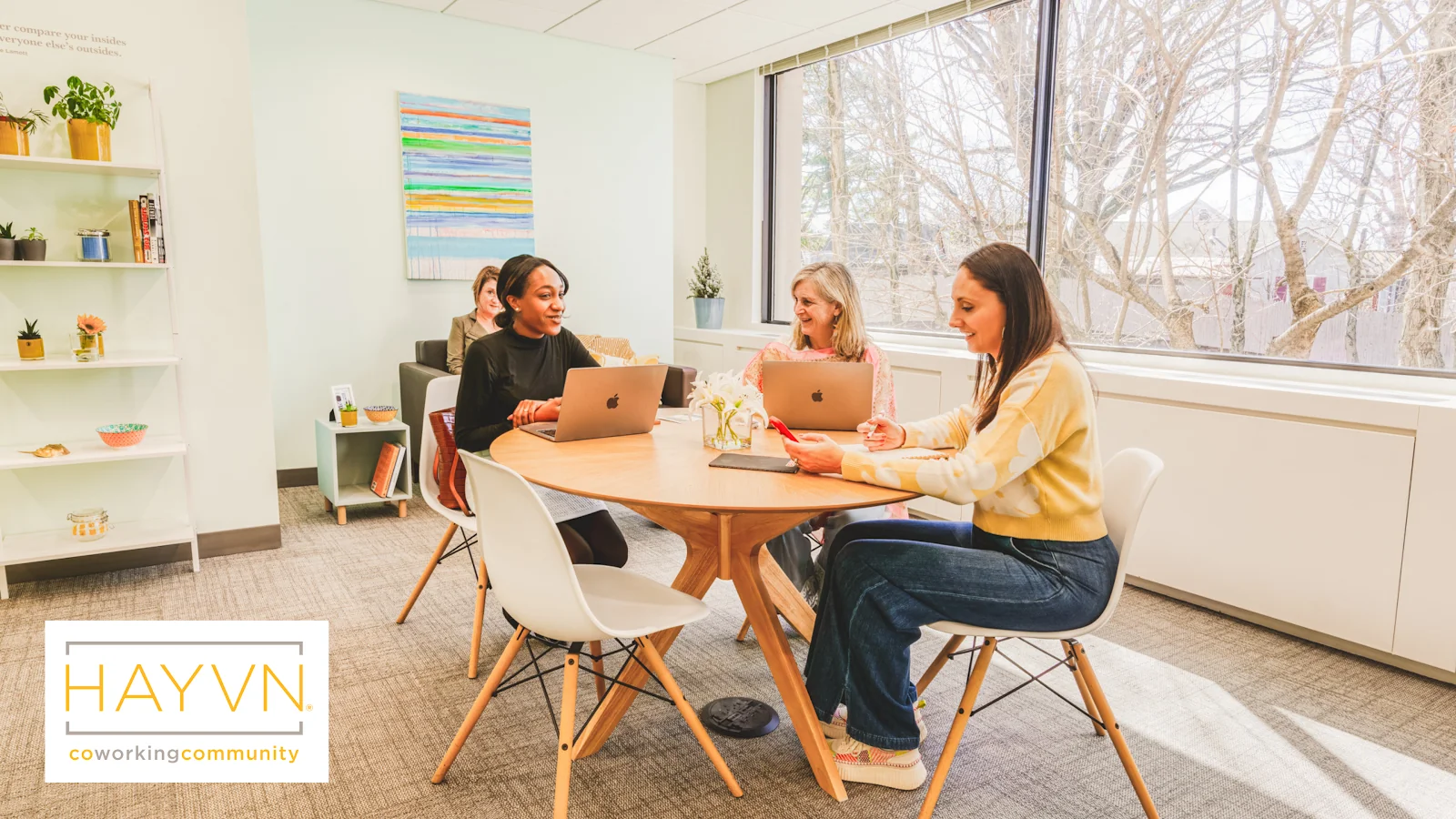 HAYVN Coworking Greenwich - women collaborating at round wood table with HAYVN branding