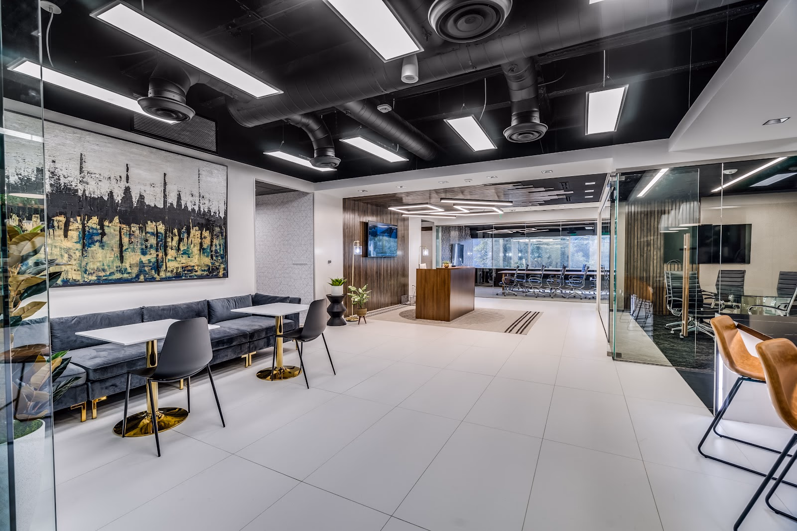 Lucid Private Offices Mockingbird Station upscale lobby with black ceiling, charcoal velvet banquette seating, gold-leg cafe tables, large abstract blue-black-gold painting, walnut reception desk, glass-walled conference rooms with executive chairs, and white tile floor