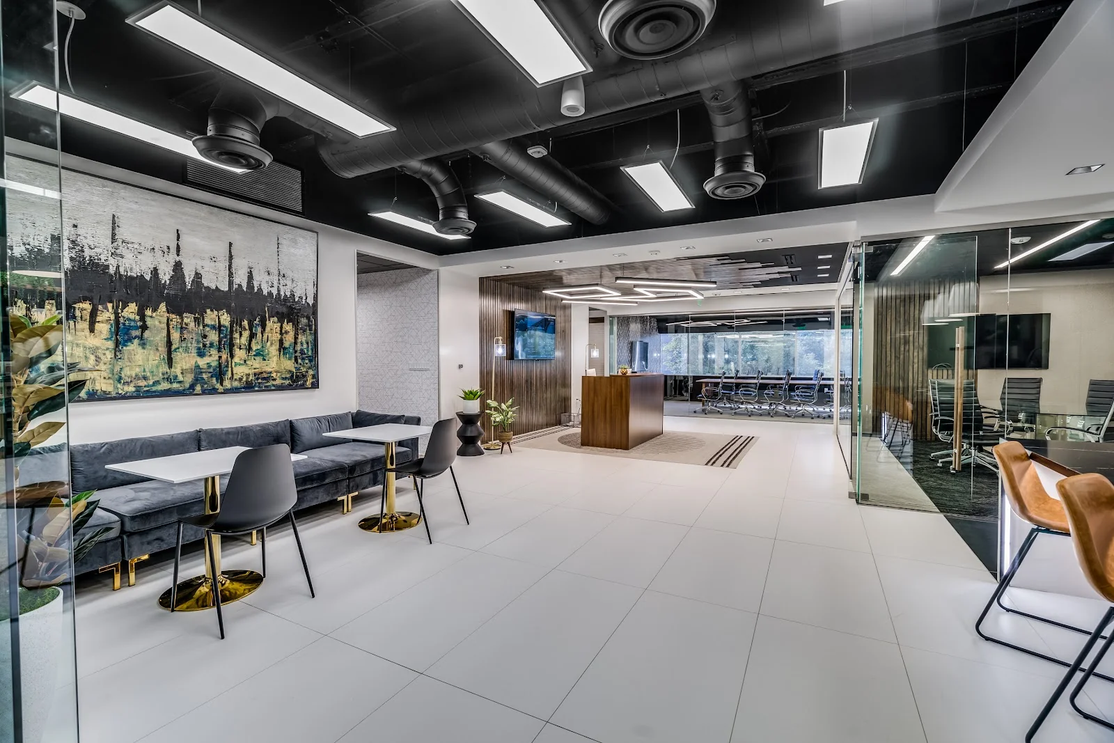 Lucid Private Offices Mockingbird Station upscale lobby with black ceiling, charcoal velvet banquette seating, gold-leg cafe tables, large abstract blue-black-gold painting, walnut reception desk, glass-walled conference rooms with executive chairs, and white tile floor