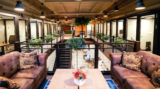 LionShare Cowork industrial two-story interior with mezzanine level, leather couches, glass-walled private offices, and plants