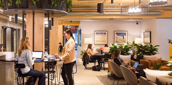 Industrious Orlando open coworking lounge with hanging greenery on wooden columns, plants, and warm lighting
