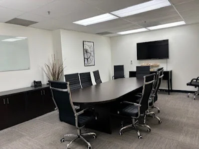 Execu-Suites conference room with oval table, black executive chairs, and wall-mounted TV