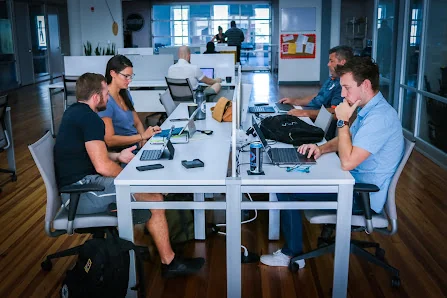 CoWork Annex open shared desk area with people working on laptops at white tables in bright natural light