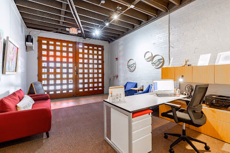 The Nest Coworking loft-style private office with red couch, wooden grid doors, white brick walls, and exposed beam ceiling