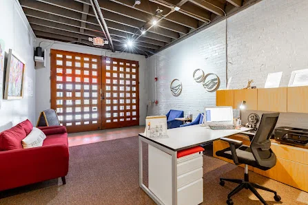 The Nest Coworking loft-style private office with red couch, wooden grid doors, white brick walls, and exposed beam ceiling