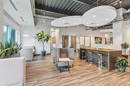 Office Evolution Jacksonville Bartram modern open lounge with hardwood floors, gray seating, bar counter, and circular acoustic ceiling panels