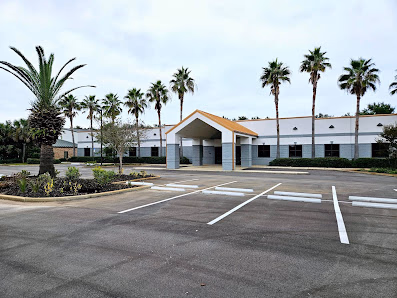 Gulf Breeze Cowork Annex single-story commercial building with peaked roof entrance, tall palm trees, and large parking lot