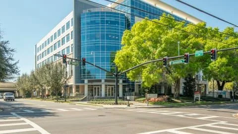 Regus Orlando GAI Building modern blue-glass multi-story office building at a street intersection with traffic lights and green trees