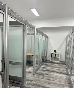 Brevard Workspace hallway of glass-partitioned private office pods with aluminum frames and minimalist white interior