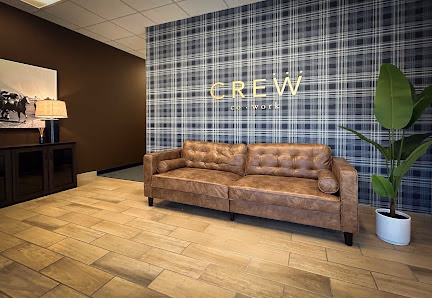 Crew CoWork welcoming lobby with tufted leather couch, blue plaid accent wall with CREW signage, and potted plant