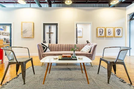 Ink CoWork stylish gallery-like lounge with blush velvet couch, mid-century coffee table, industrial metal chairs, and portrait artwork on walls