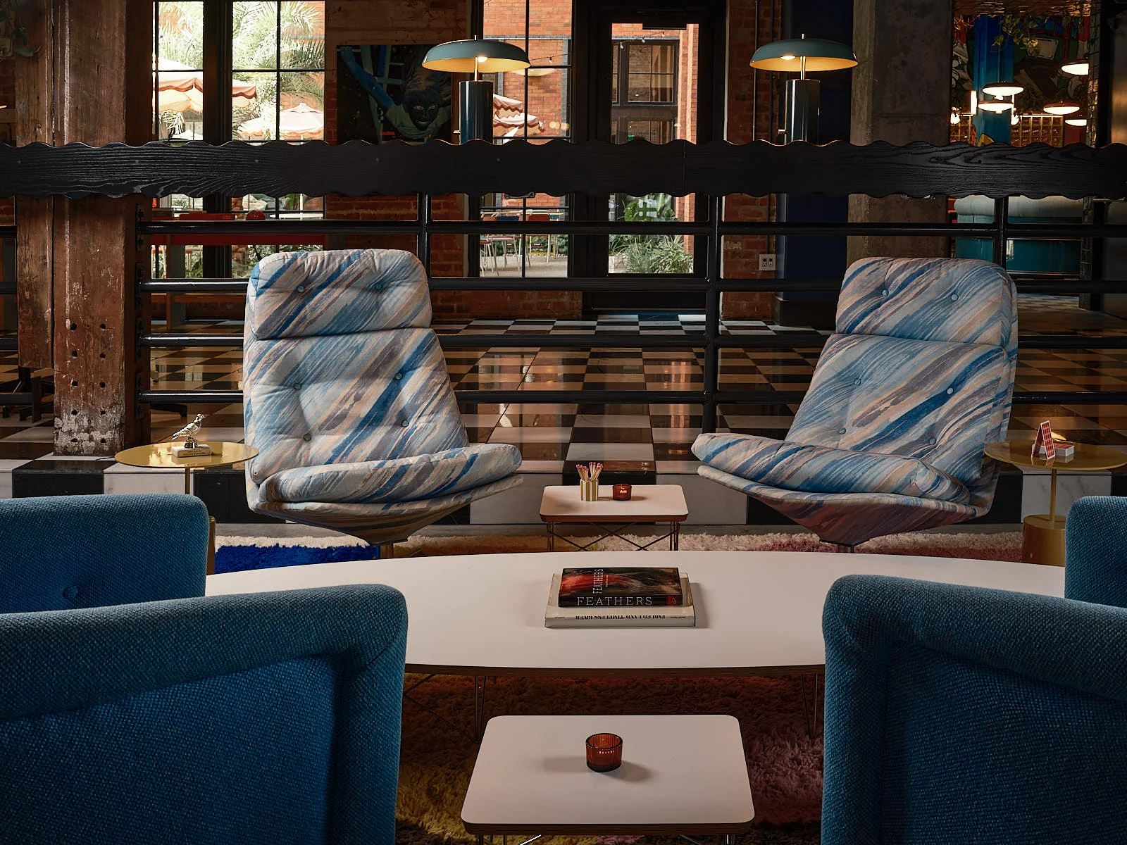 Common House New Orleans upscale lounge with blue marble-swirl tufted chairs, checkered floor, teal armchairs, and dark scalloped wood divider