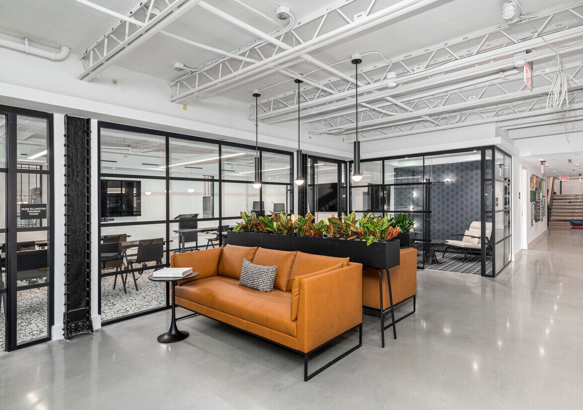 Venture X coworking space in Washington DC featuring industrial glass-walled offices, orange leather sofa, and polished concrete floors