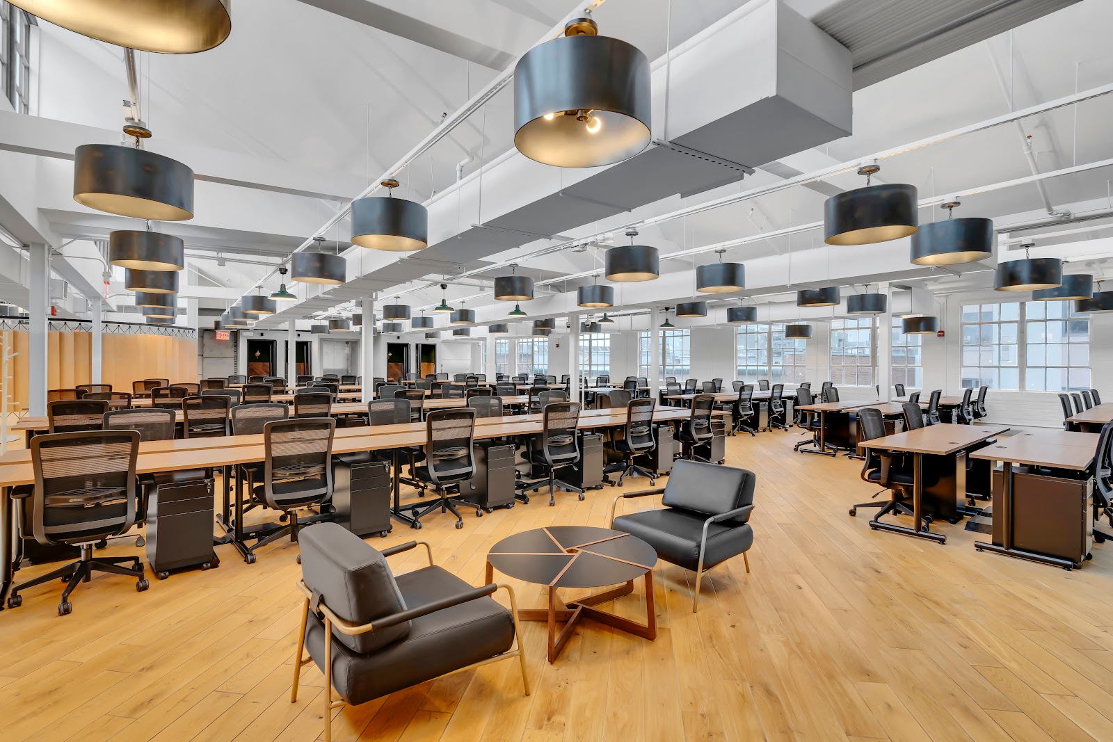 The Mark Manhattan Laundry open workspace with black and gold drum pendant lights, rows of desks, and hardwood floors in converted historic building