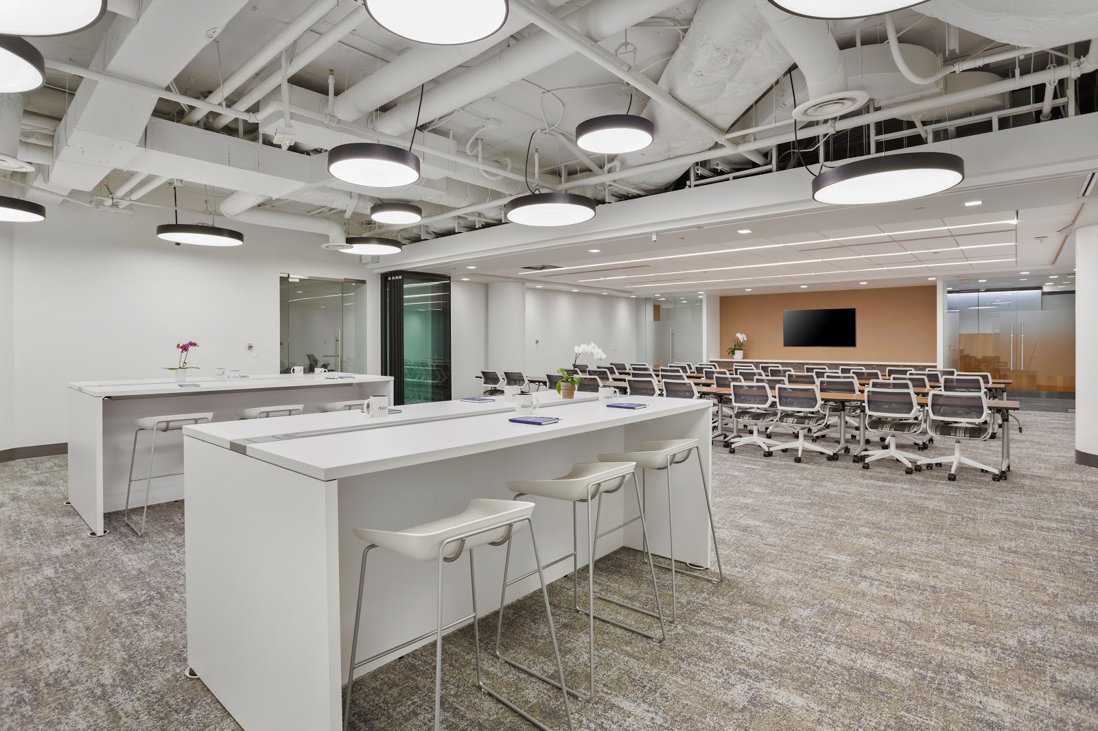 District Offices Pennsylvania Avenue white modern event space with round pendant lights, bar tables, and peach accent wall