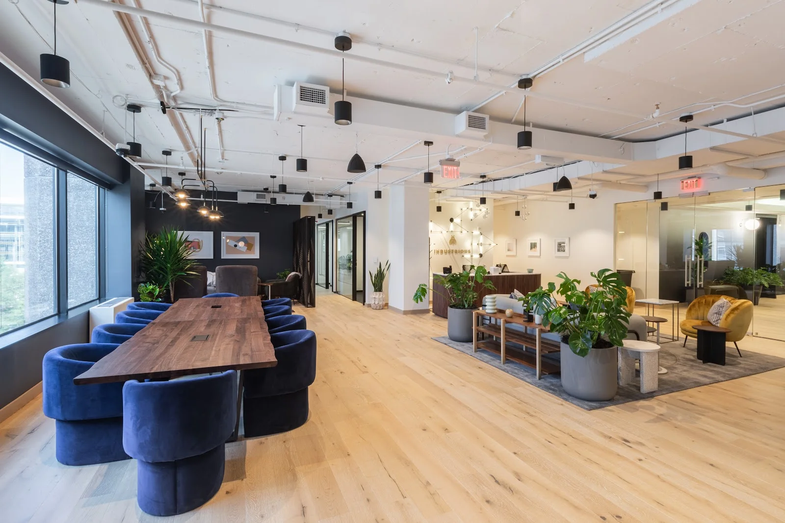 Industrious Mass Ave lounge with navy velvet chairs around walnut communal table, light hardwood floors, and abundant greenery