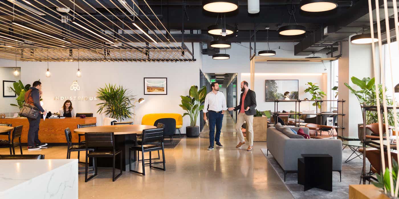 Industrious Thomas Circle welcoming lobby with Industrious branding, people chatting, yellow accent chair, plants, and polished concrete floors