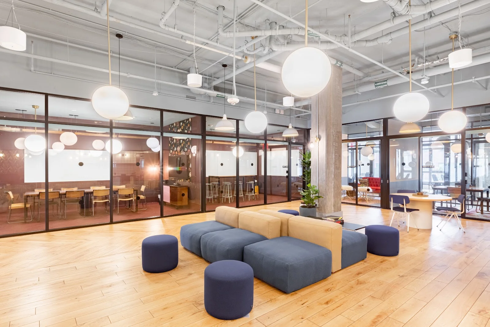 Industrious H Street open lounge with modular blue and beige sofas, poufs, white globe pendant lights, and glass-walled offices