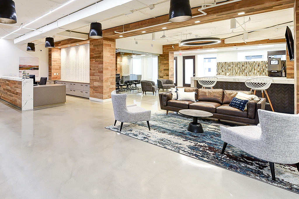 Premier Workspaces lobby with reclaimed wood accent walls, brown leather sofa, gray armchairs, mosaic coffee bar, and polished concrete floors