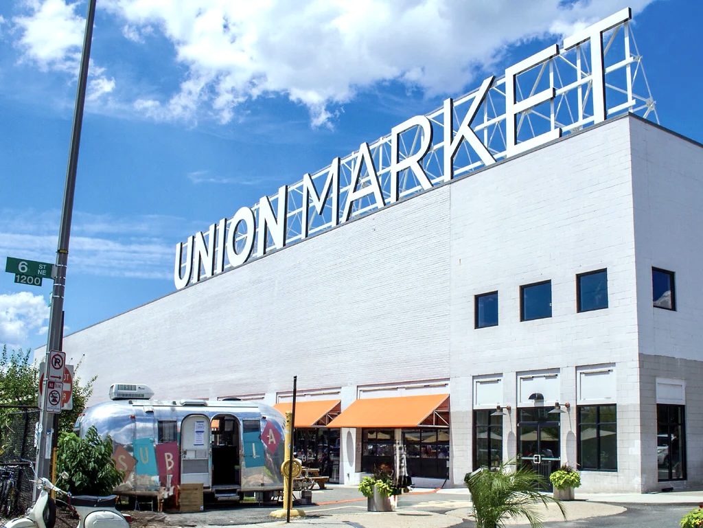 Enclave Coworking at Union Market white industrial building exterior with large rooftop signage, Airstream trailer, and orange awnings