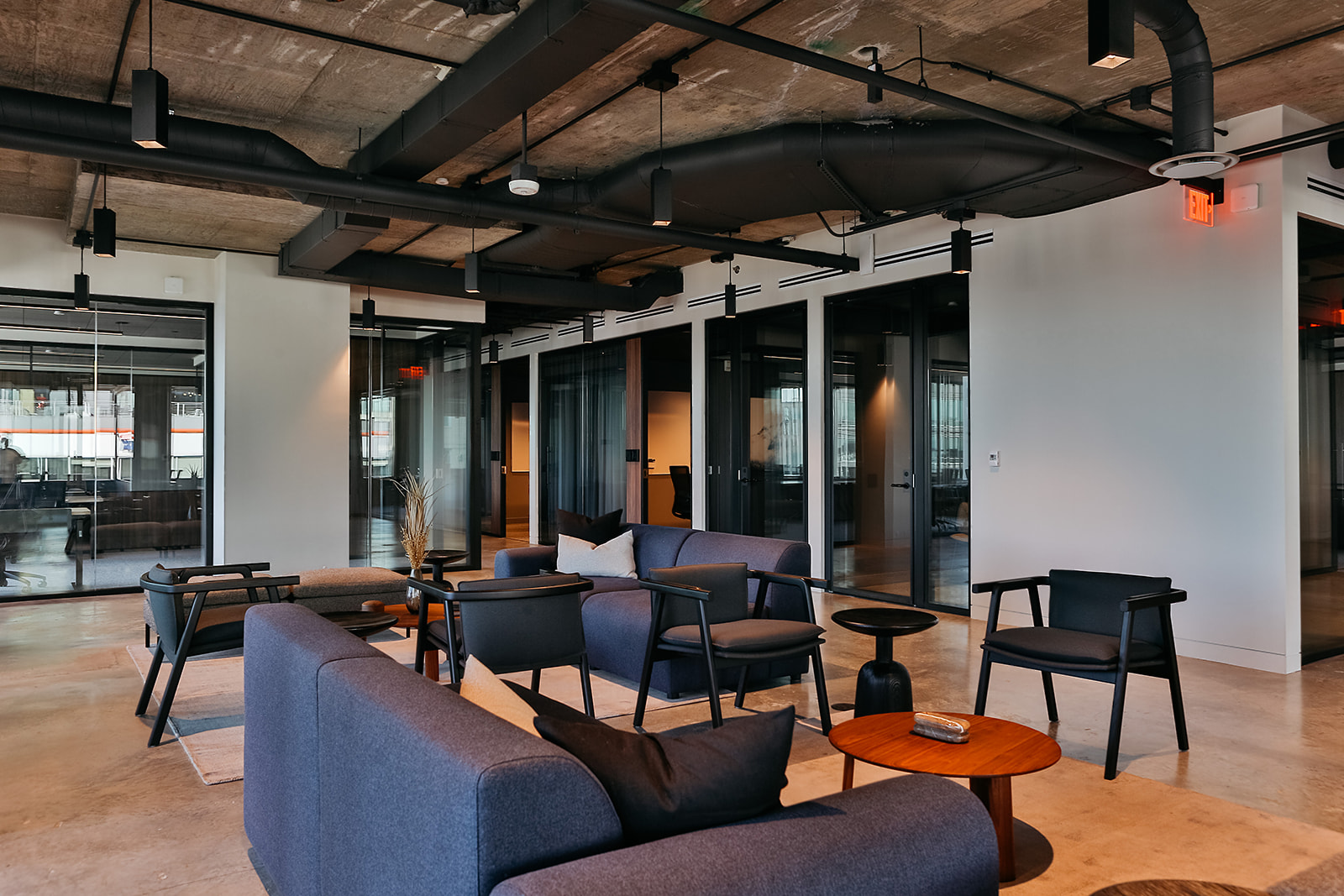 Launch Workplaces Navy Yard industrial-modern lounge with charcoal sofas, black armchairs, exposed concrete ceiling, and glass-walled private offices