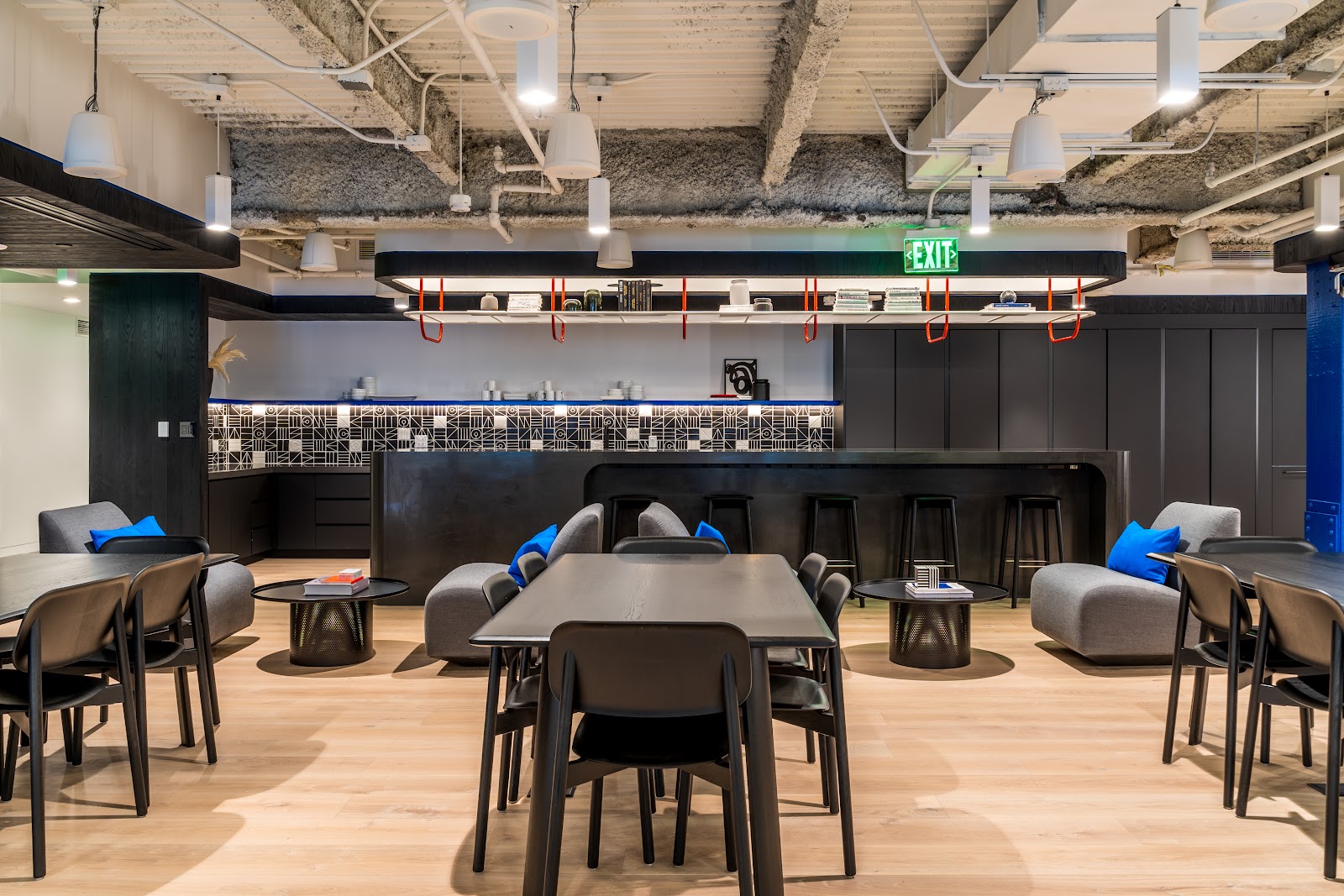 CommonGrounds dark industrial-chic lounge with black tables, gray seating with blue accent pillows, geometric tile backsplash, and light hardwood floors