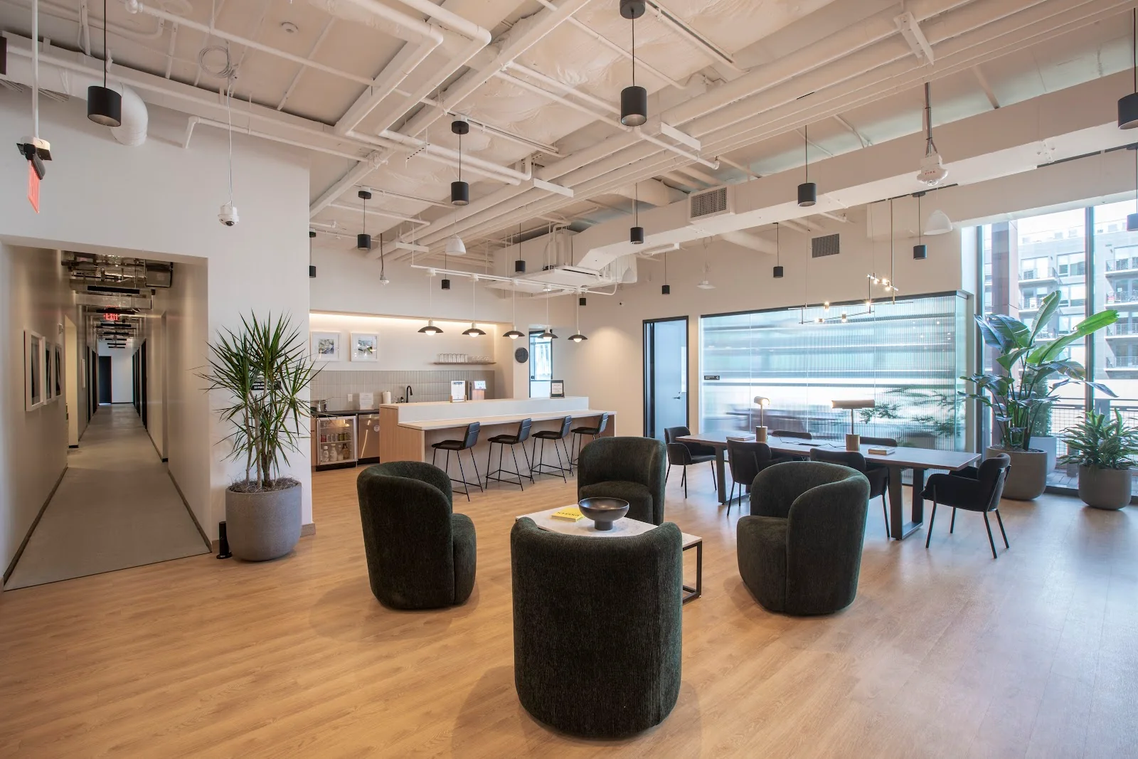 Industrious Union St modern lounge with dark green swivel chairs, kitchen bar with stools, light hardwood floors, and large windows with city views