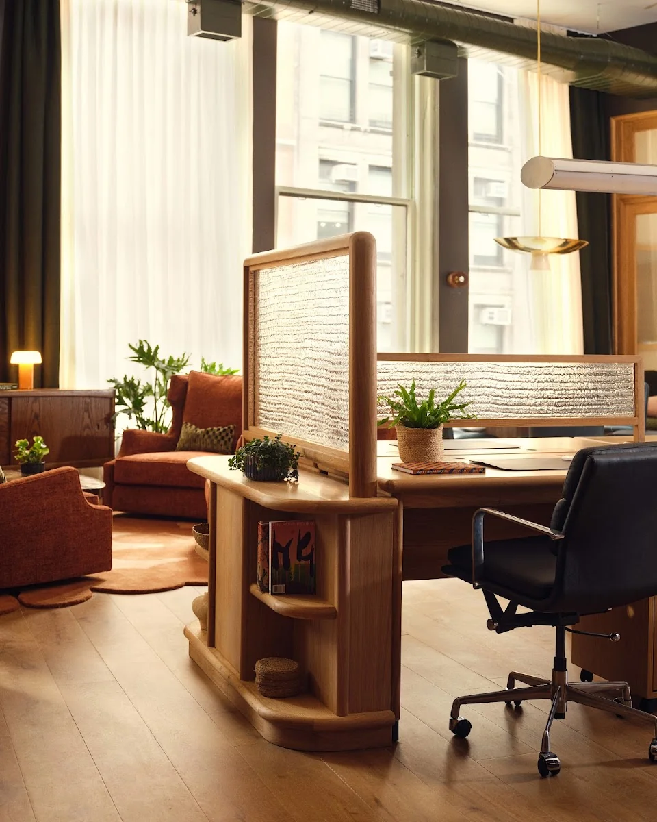 The Malin DC boutique workspace with wooden desk divider, woven panel, black leather Eames chair, terracotta sofa, and warm natural light